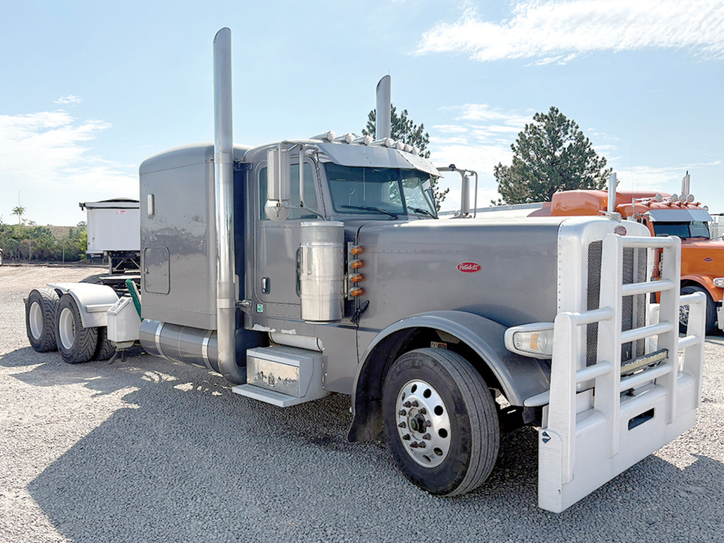 Peterbilt 389 extended hood truck viewed from passenger side front; chrome exhaust stacks, large front bumper guard, silver cab with air intake, dual rear wheels, visible front wheel and grille badge