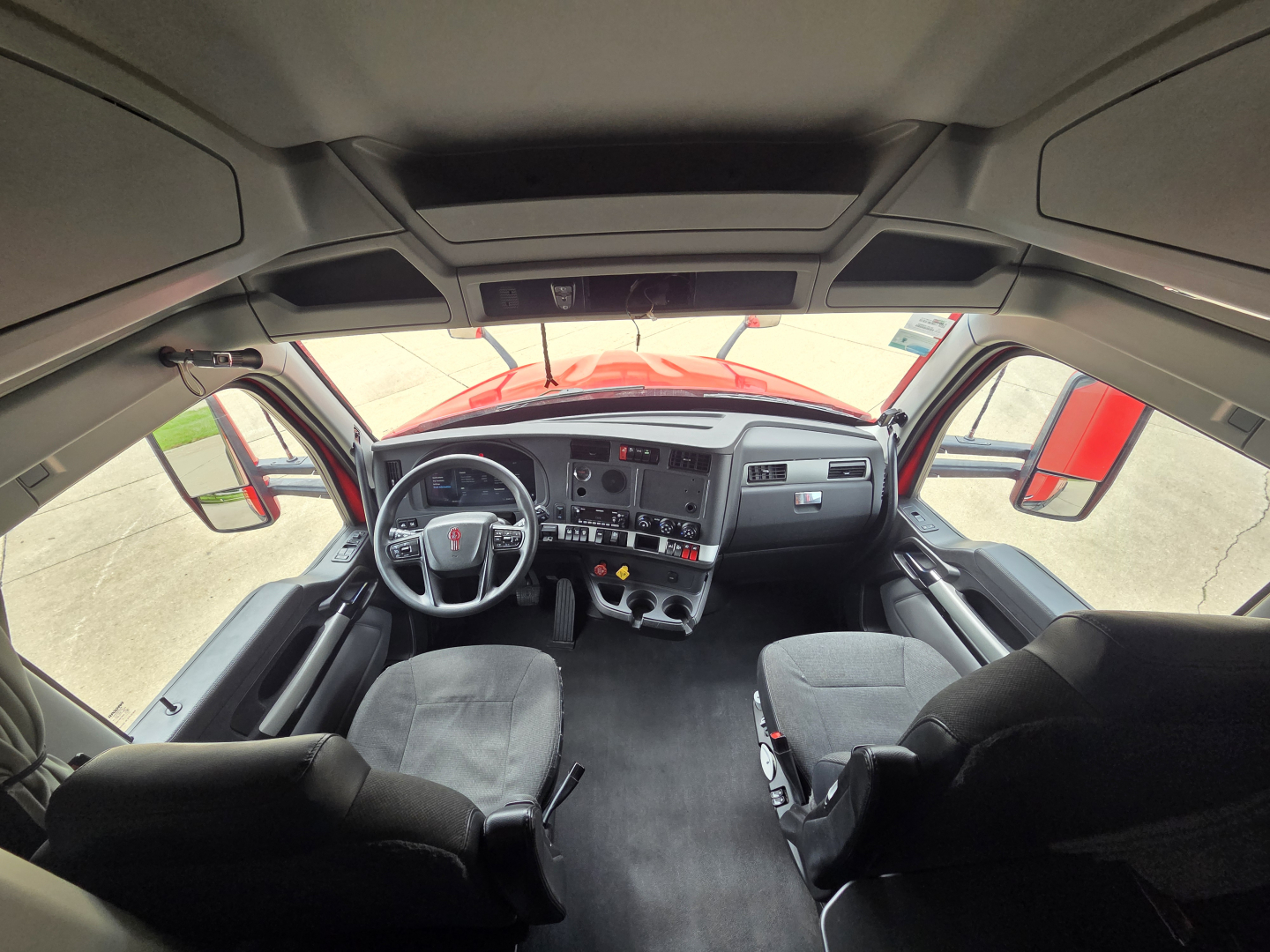 Kenworth T680 cab interior showing steering wheel, dashboard, and two front seats. No legible text visible on panels in image.