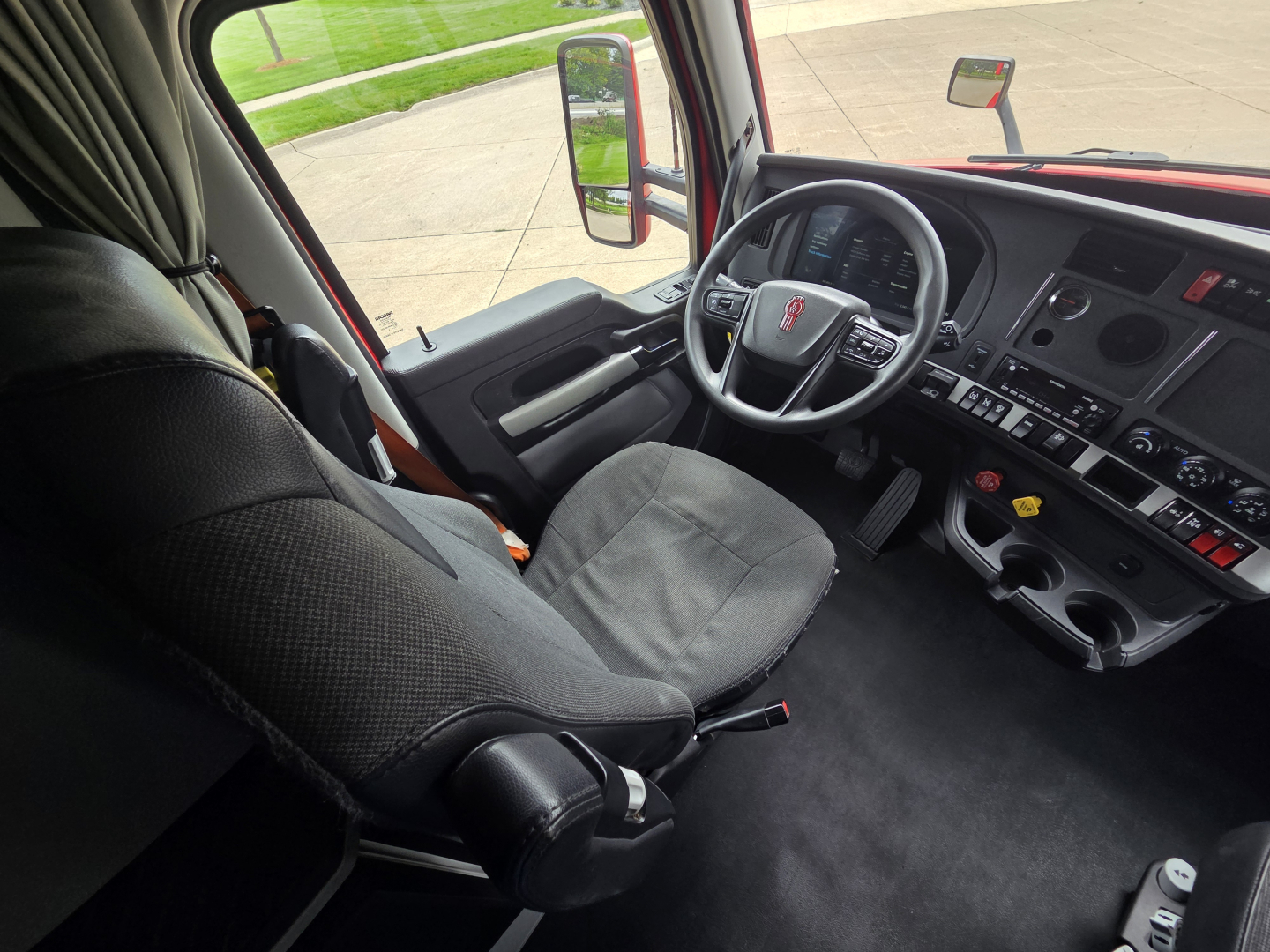 Vehicle cab interior of a 2023 Kenworth T680, driver seat and dashboard visible with steering wheel, console controls, and side window.