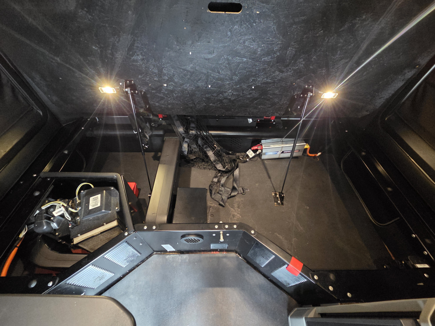 Truck cab interior view showing storage area under sleeper with wiring, panels, and support rods; illuminated under-cab lighting on both sides.