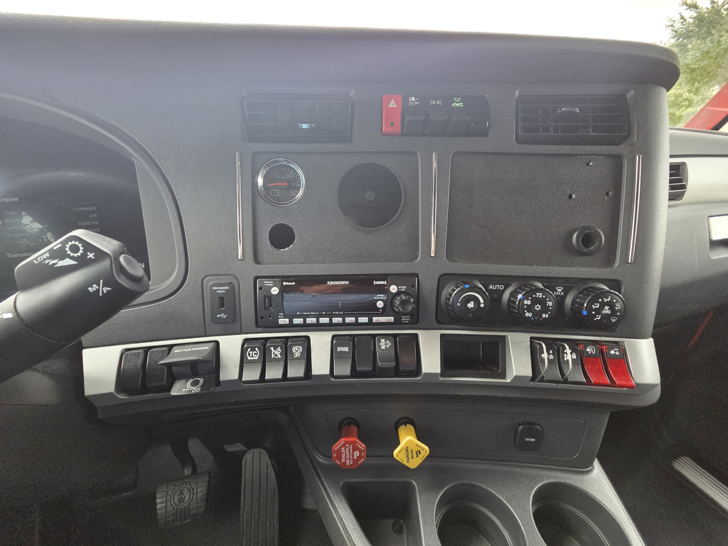 Kenworth T680 dash/console showing center controls, gauges, switches, two colored hazard levers, and radio panel.