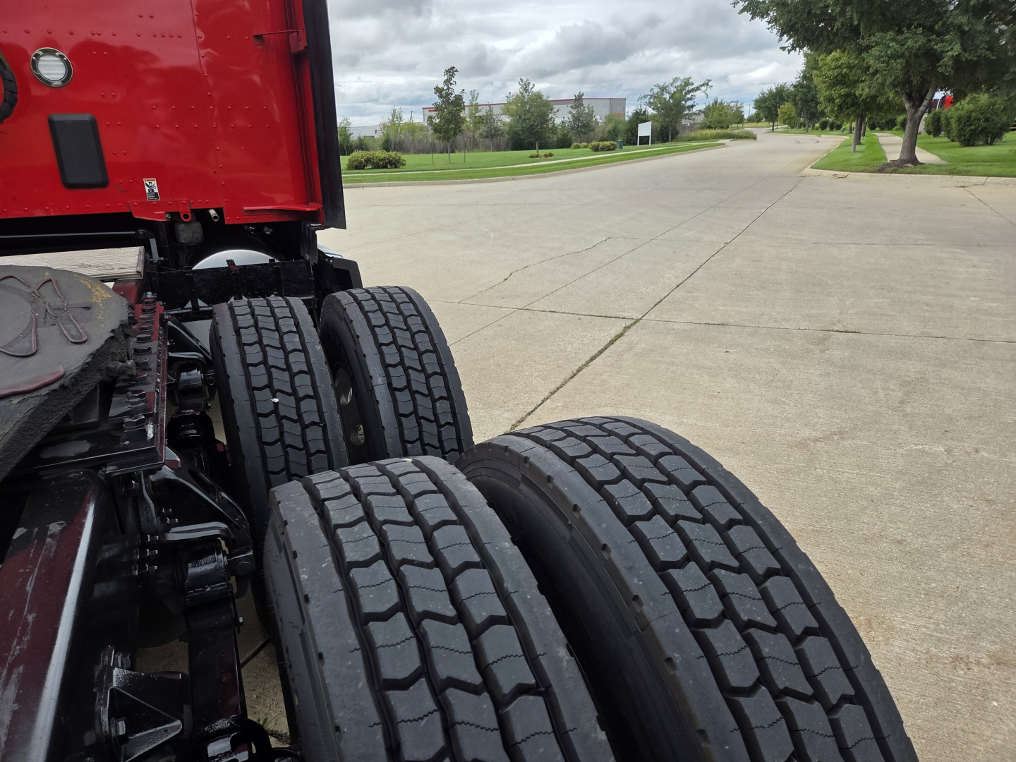 Kenworth truck rear dual tires and red cab with visible undercarriage; shows wheel assembly and part of chassis.