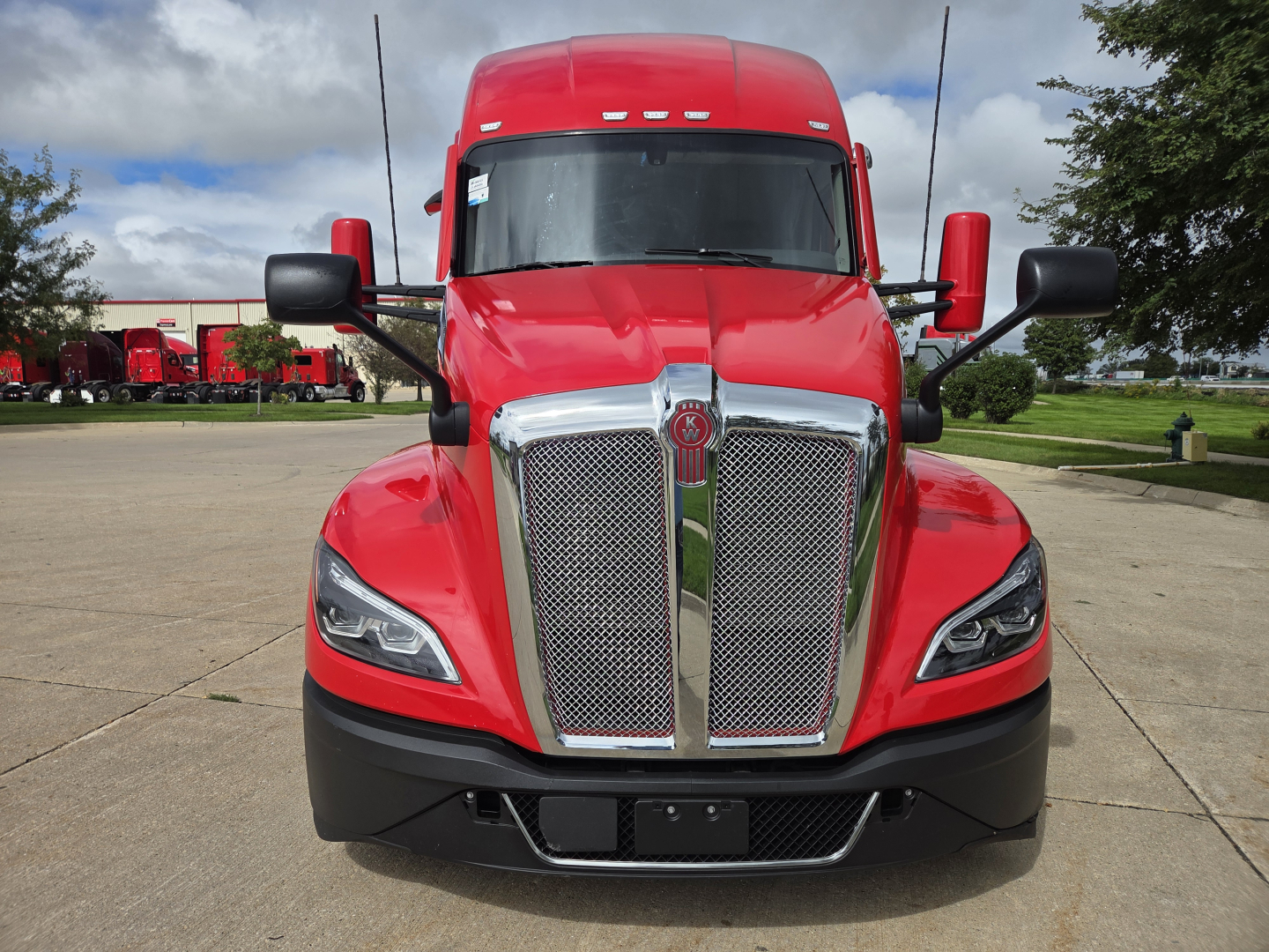 Kenworth T680 truck front view showing aggressive chrome grille and red cab, black bumper, and large mirrors.