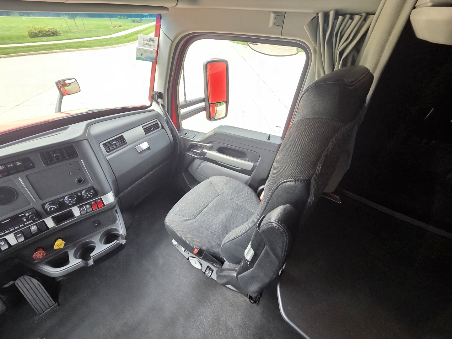 Kenworth truck interior cab view with driver seat and dashboard; visible are steering column, pedal set, and control panel.