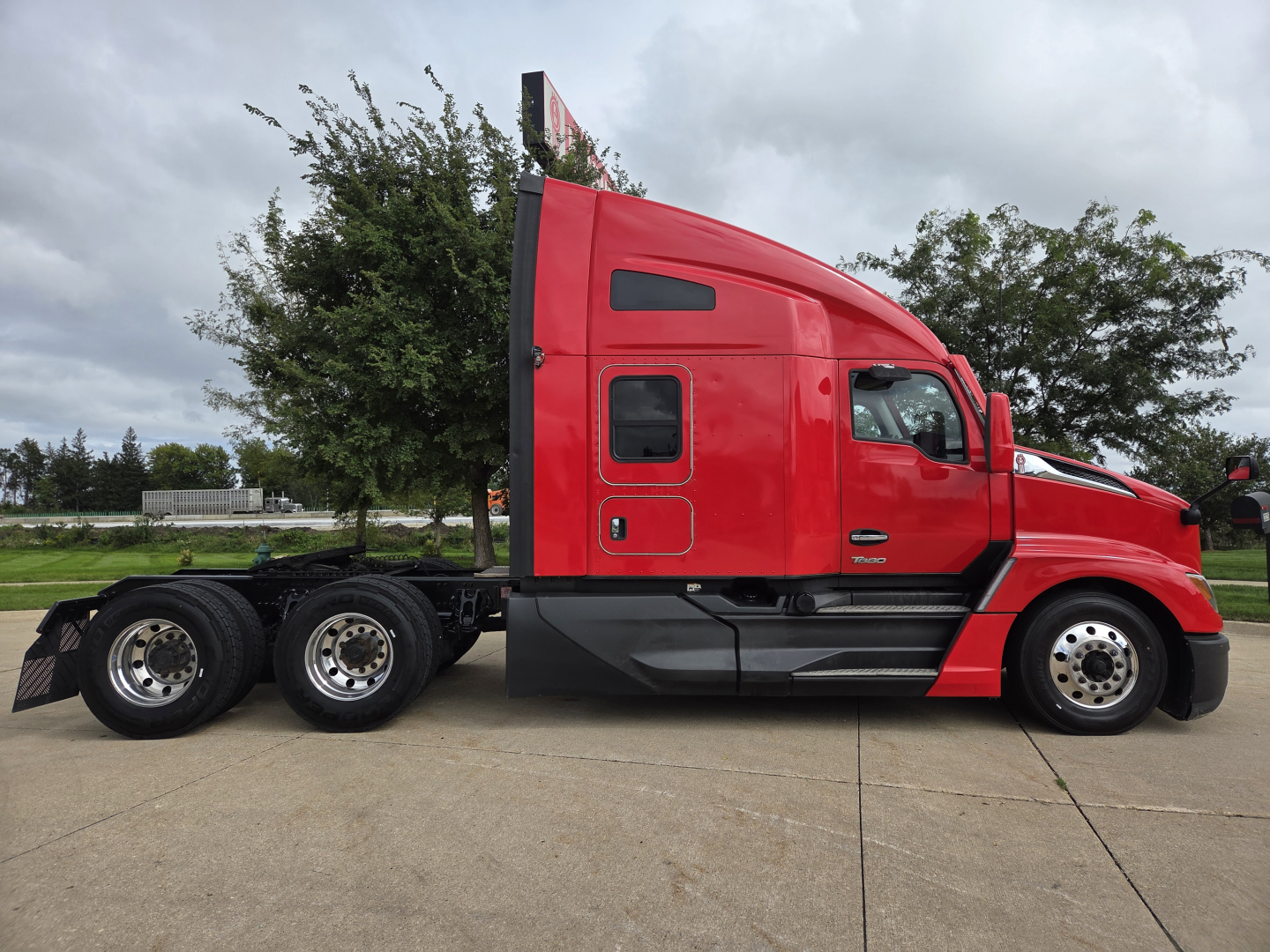 Kenworth T680 side view showing red sleeper cab and chassis with multiple rear axles.