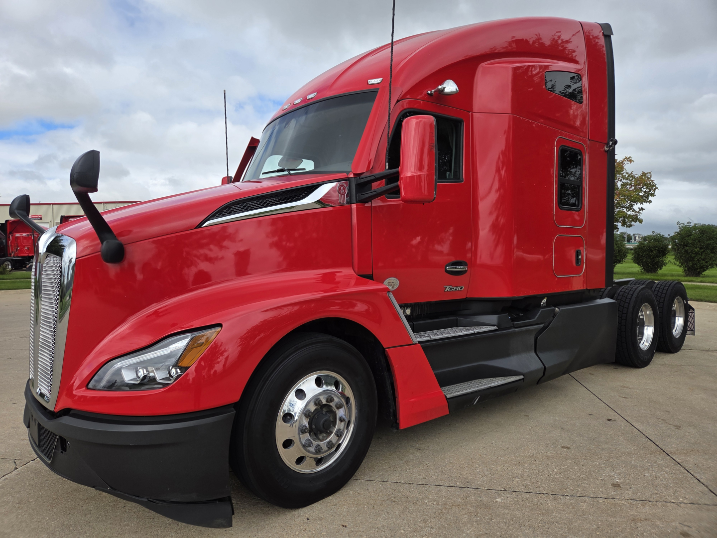 Kenworth T680 red semi-truck side view showing cab and front wheel, sleeper configuration, chrome fuel tanks, and dual rear axles.