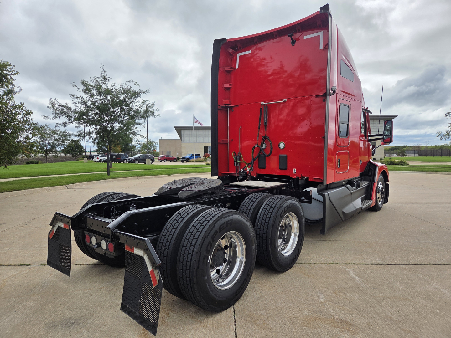 Kenworth T680 truck rear/side view showing dual rear axles and red sleeper cab. Visible text on side window and rear door includes no legible model text due to angle.