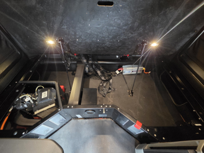 Truck cab interior view showing storage area under sleeper with wiring, panels, and support rods; illuminated under-cab lighting on both sides.