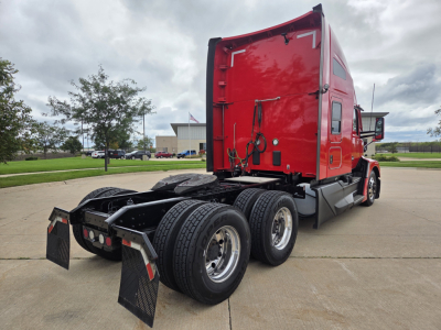 Kenworth T680 truck rear/side view showing dual rear axles and red sleeper cab. Visible text on side window and rear door includes no legible model text due to angle.