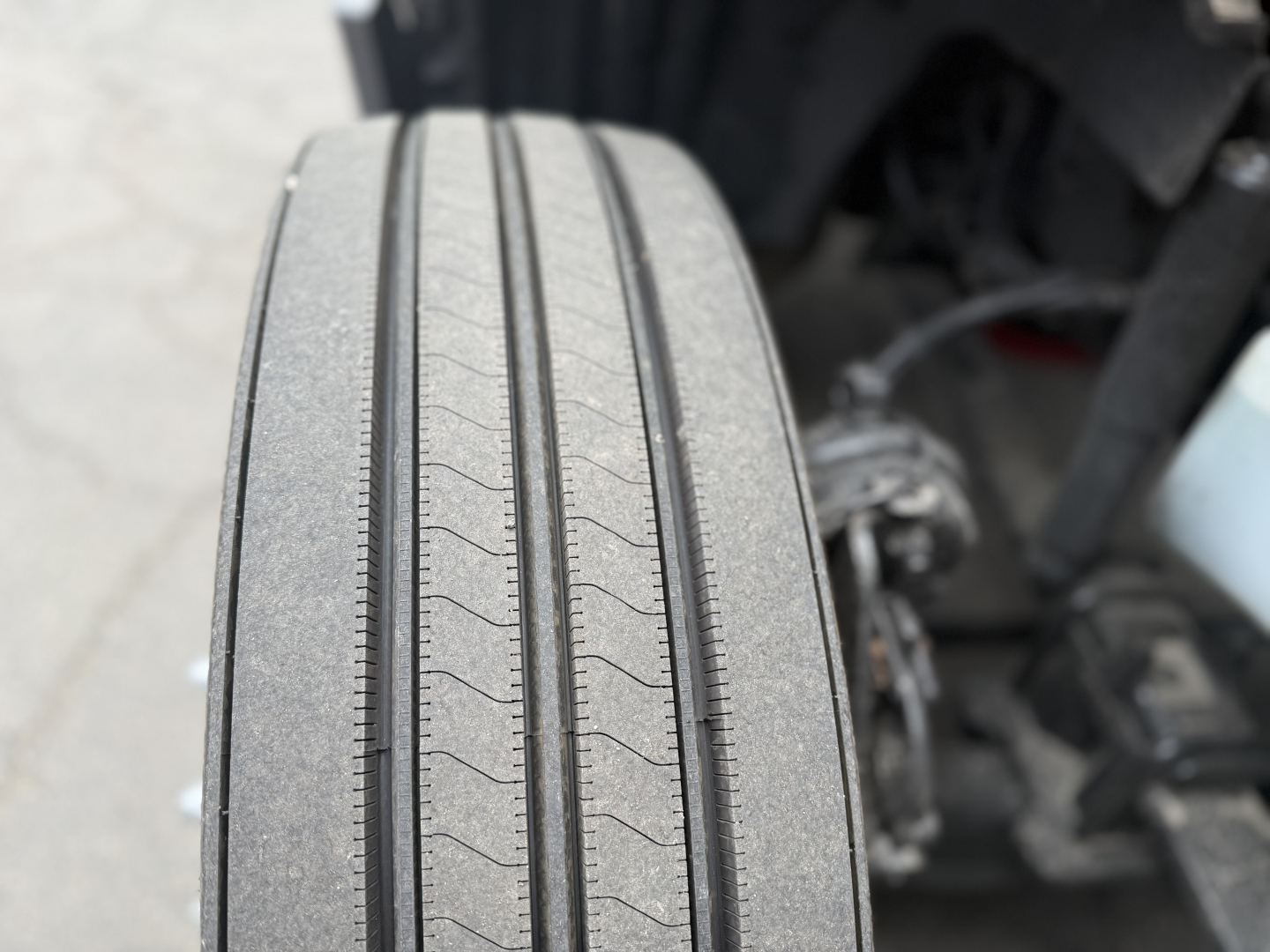Tires on a truck front view with tread pattern visible; close-up of wheel well and suspension components in background.