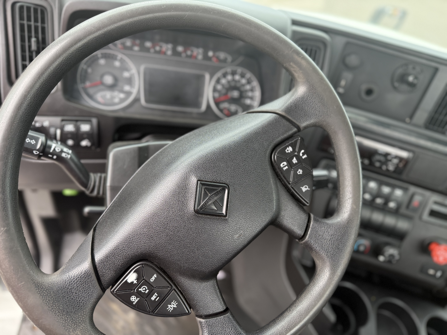 Truck steering wheel with center logo, dashboard gauges in background, controls on left and right of steering wheel visible.