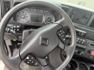 Truck steering wheel with center logo, dashboard gauges in background, controls on left and right of steering wheel visible.