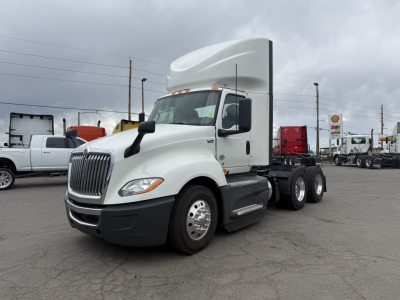 Truck cab and trailer chassis showing International LT625 daycab with white exterior and sleeper aerodynamic top, front grille, and dual rear axles.