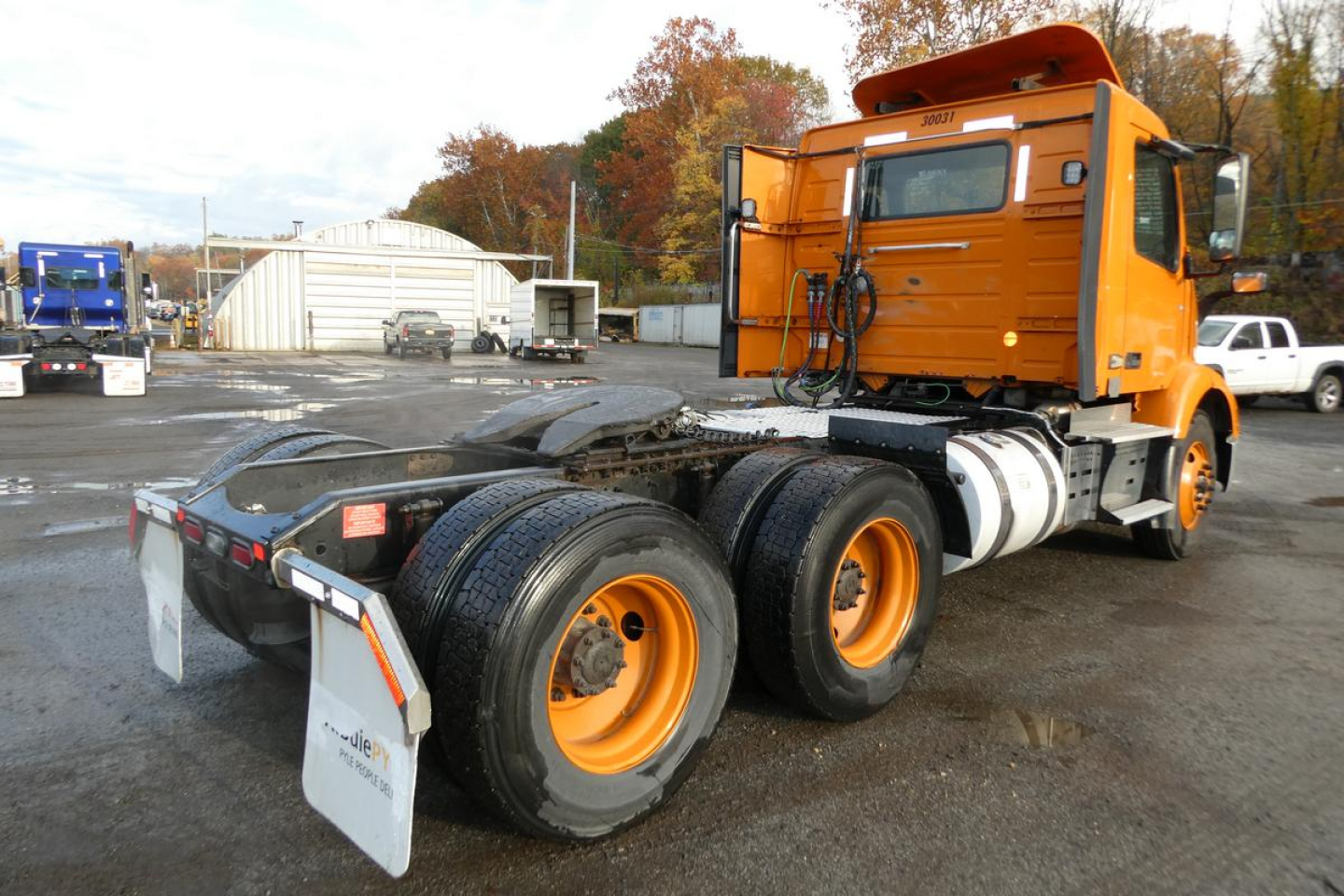 Volvo VNR truck tractor chassis rear view showing orange cab and dual rear axles with yellow wheels and tires.