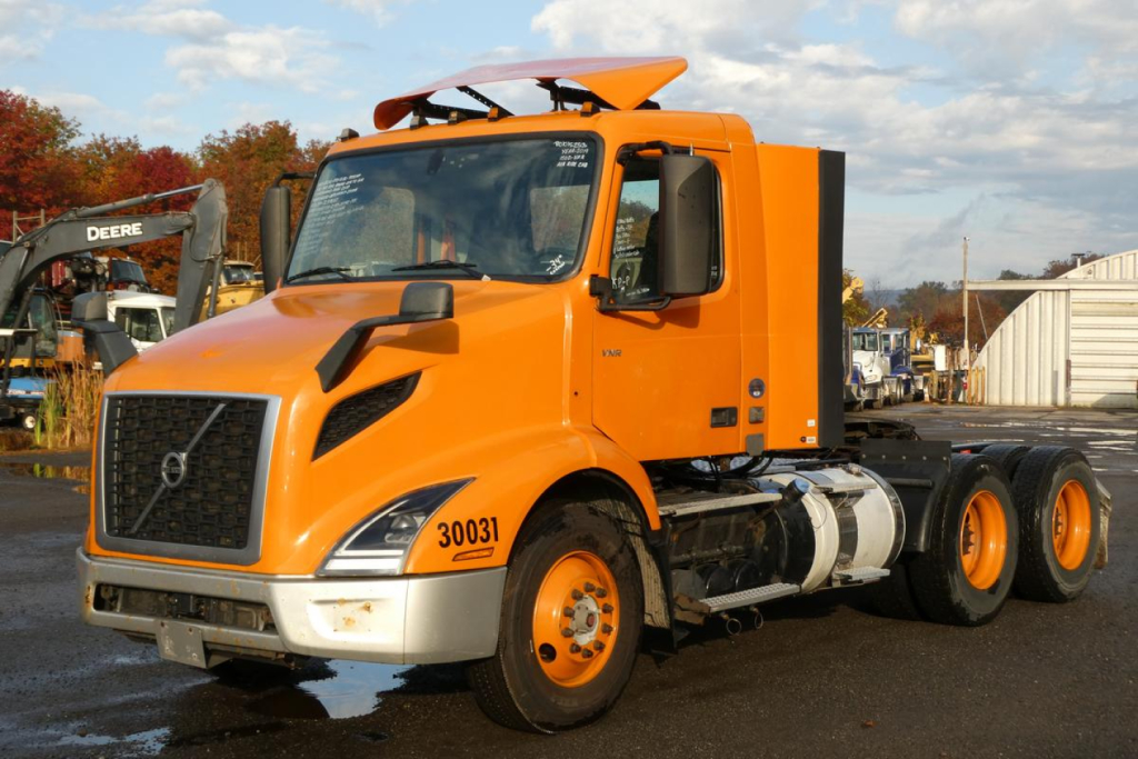 Orange Volvo VNR64T300 day cab tractor truck side view showing cab roof fairing and dual rear axles.