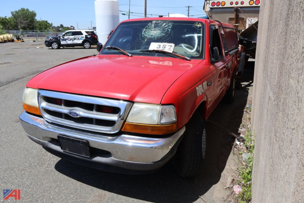 Red 1999 Ford Ranger pickup truck front-left view with price tag in windshield and a white truck behind.