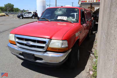 Red 1999 Ford Ranger pickup truck front-left view with price tag in windshield and a white truck behind.
