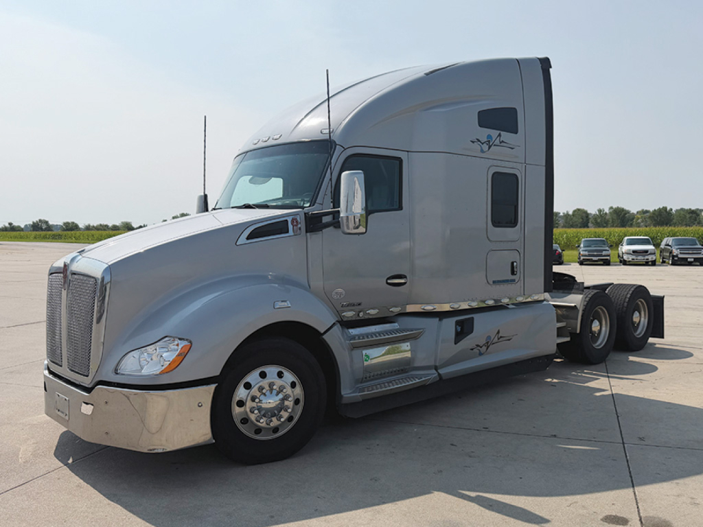 Kenworth T680 tractor in side view showing cab and chrome fuel tanks with logos on gray paint.