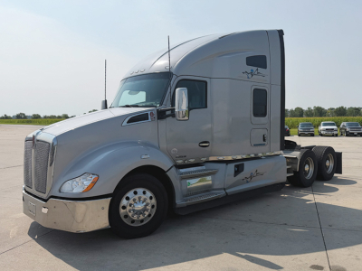 Kenworth T680 tractor in side view showing cab and chrome fuel tanks with logos on gray paint.