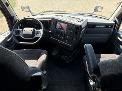 Mack PR64T76H truck cab interior showing steering wheel with Mack logo, dashboard with multiple controls, center console, and driver and passenger seats.