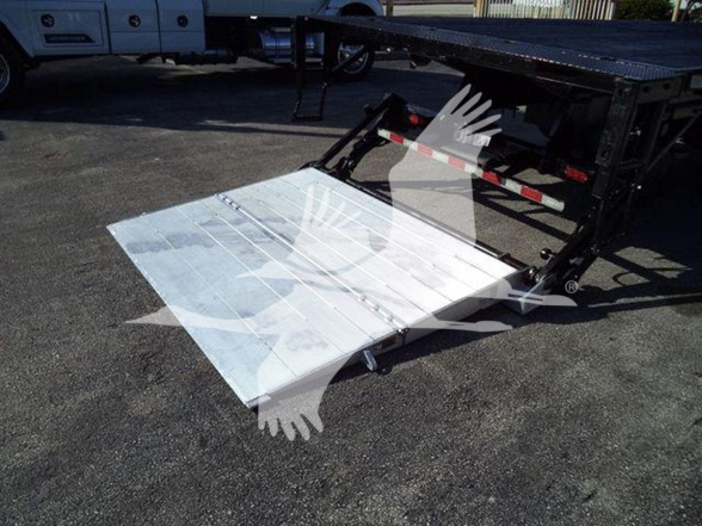 Flatbed truck with lowered aluminum ramp showing cargo bed and hydraulic mechanism.