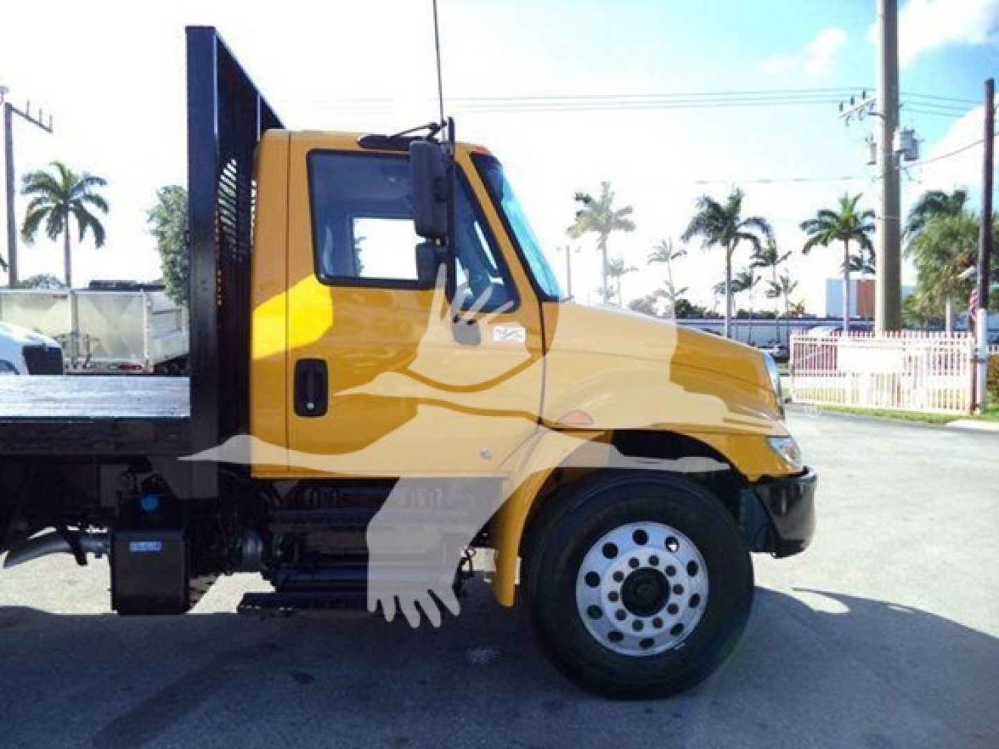 Flatbed truck side view showing 2019 International Durastar 4300 with yellow cab, black chassis, and flatbed. VIN 1HTMMMML1KH584272 visible in listing metadata.