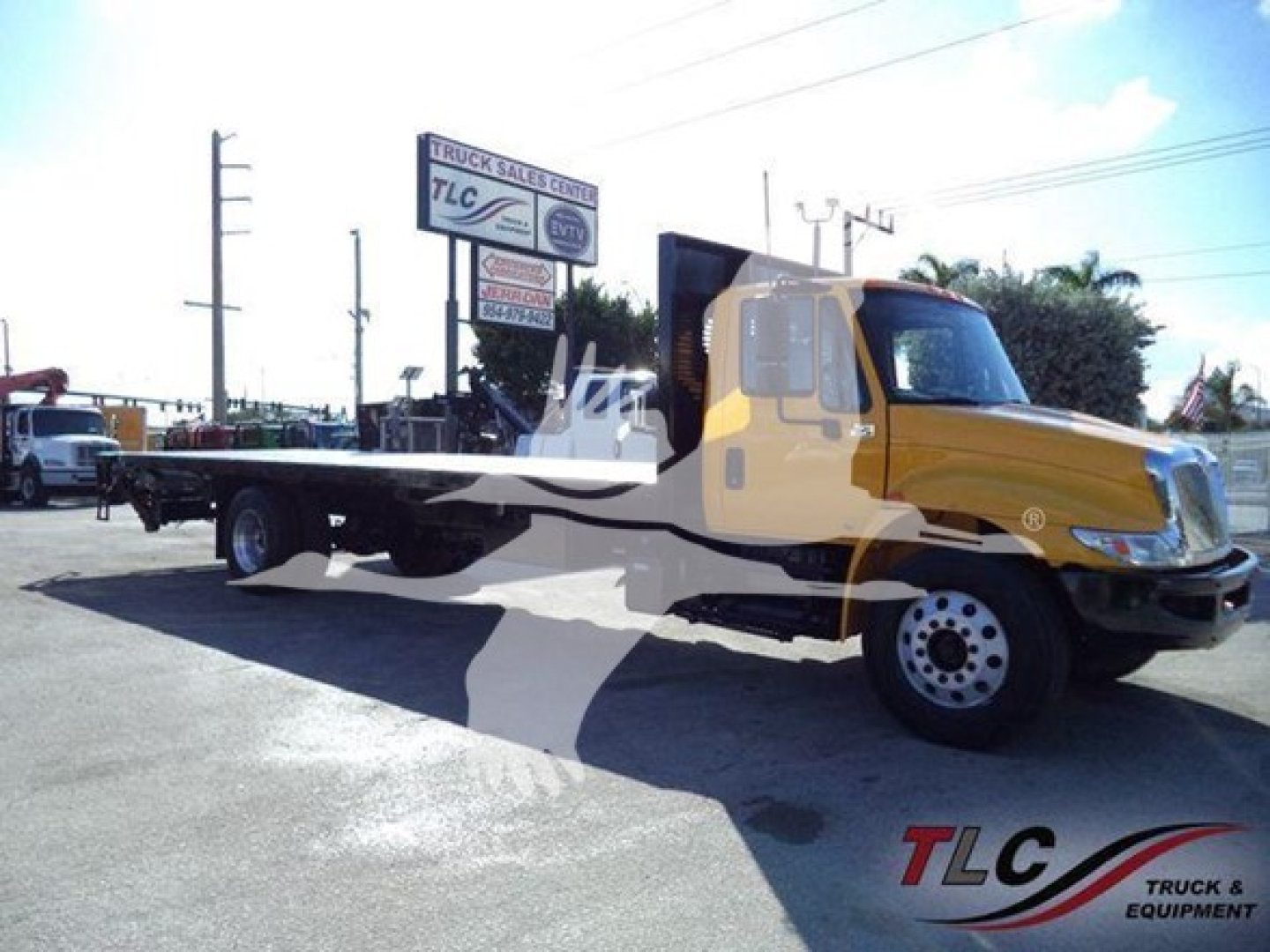 2019 International Durastar 4300 flatbed truck side view with CDL windows and yellow cab; text on sign in background is indistinct.