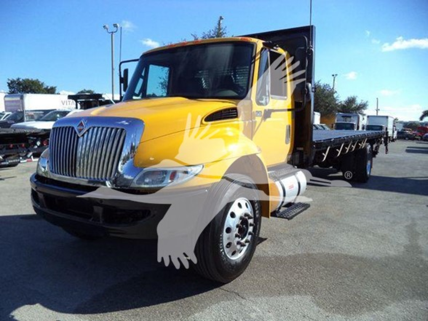 Flatbed truck shows a yellow 2019 International Durastar 4300 with a chrome grille and open cargo bed, front-left view.