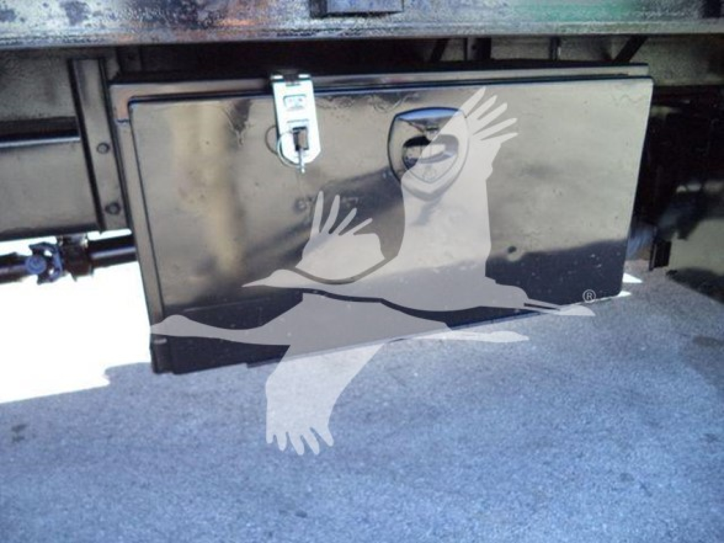 Storage toolbox mounted under truck with latch on a flatbed; metallic rectangular box with lock.