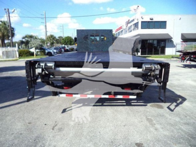 Flatbed truck attachment showing hydraulic hoist in central position and frame rails on a paved lot.