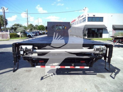 Flatbed truck rear view showing dual hydraulic ramps and carrier arms on a 2019 International Durastar 4300, with license-plate area and reflective striping.