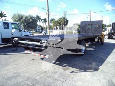 Flatbed truck in-service showing front hitch assembly and long aluminum deck with black frame in a lot.