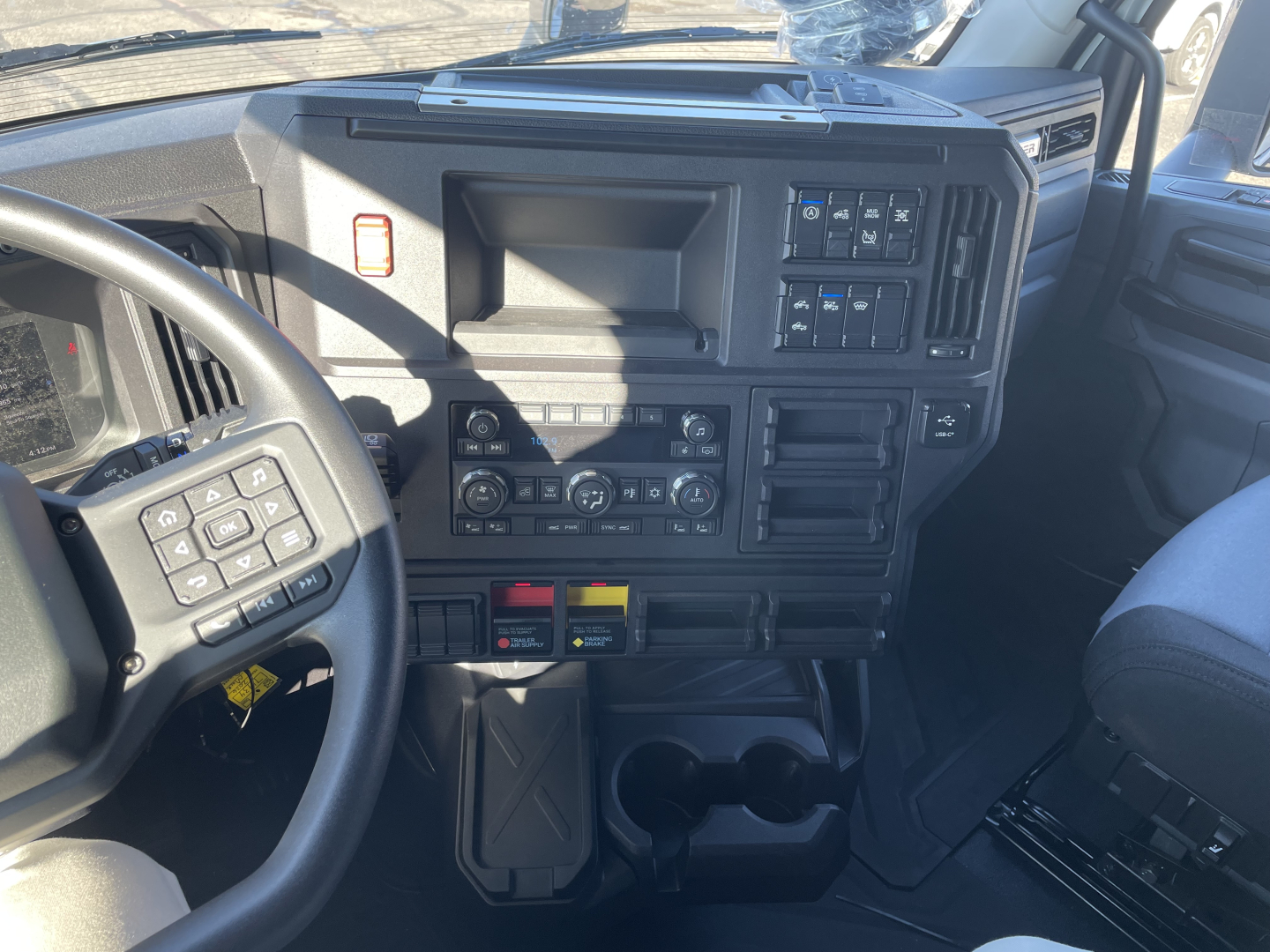 Cab interior of a 2026 Mack PR64T76H truck showing dashboard controls and steering wheel with various switches and cup holders.