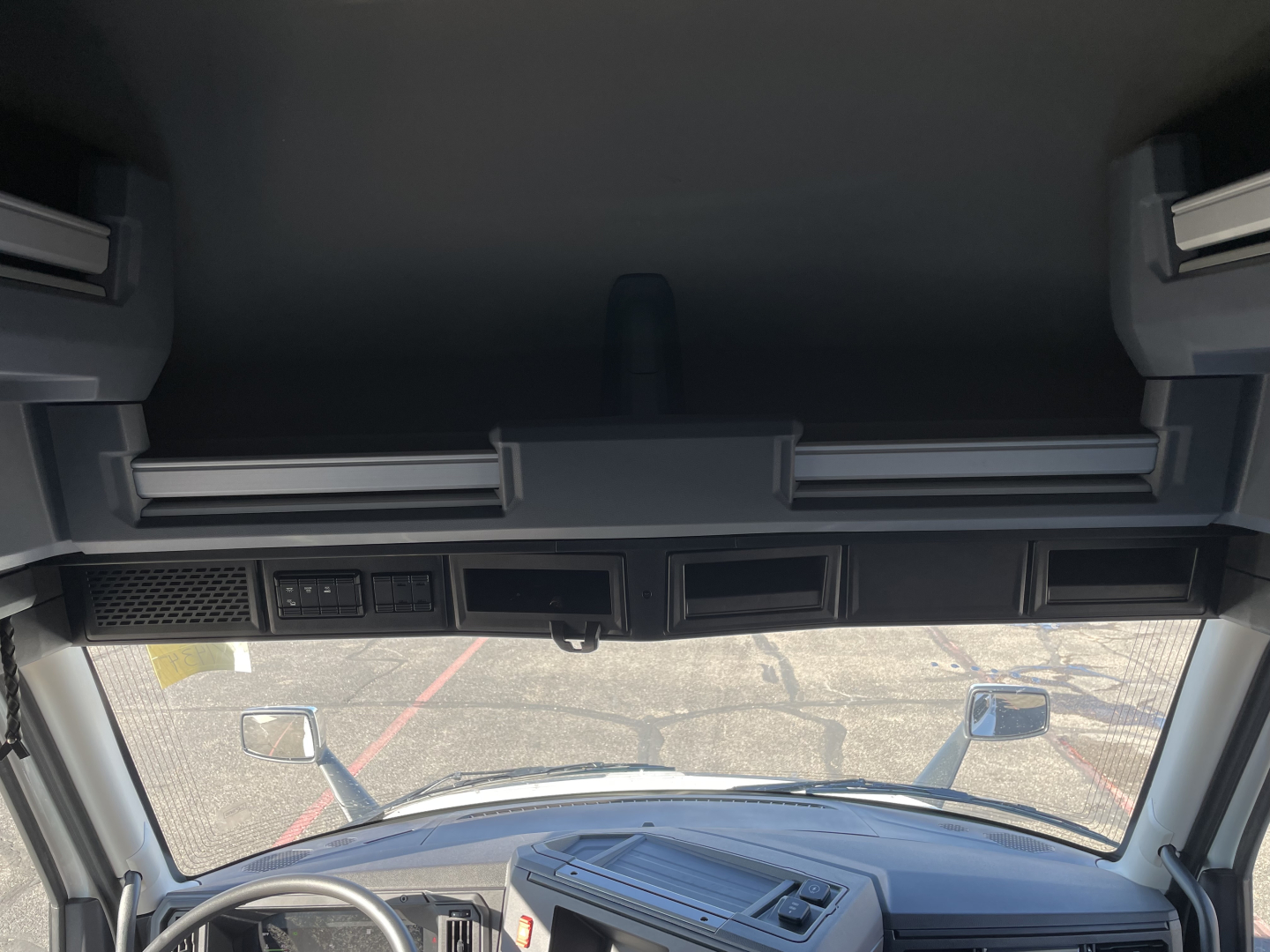Cab interior view of a new Mack PR64T76H sleeper truck showing dash area and windshield, with side mirrors and overhead storage panels.