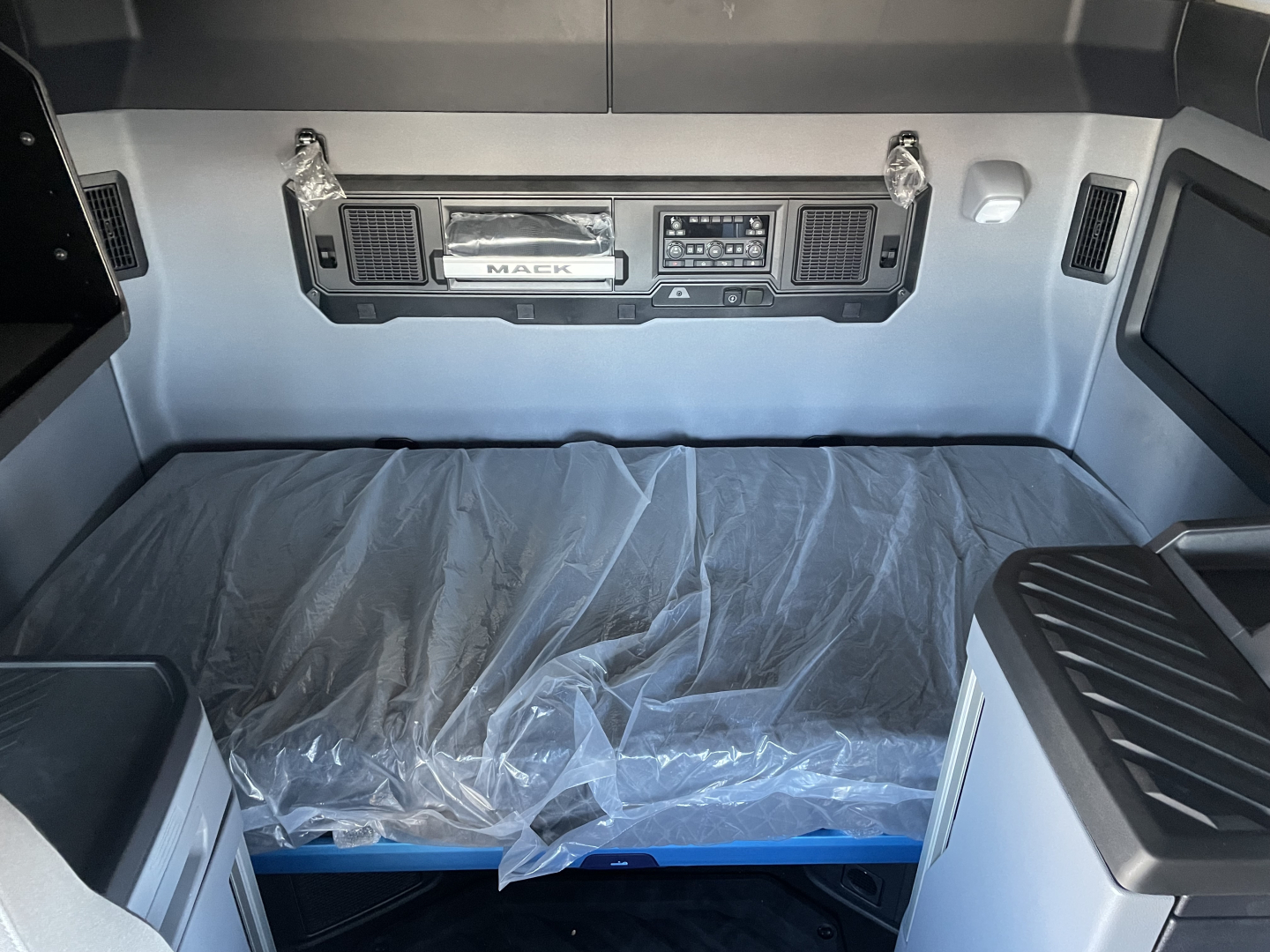 Mack PR64T76H truck interior sleeper cab cargo area with control panel at headboard and plastic-covered mattress.