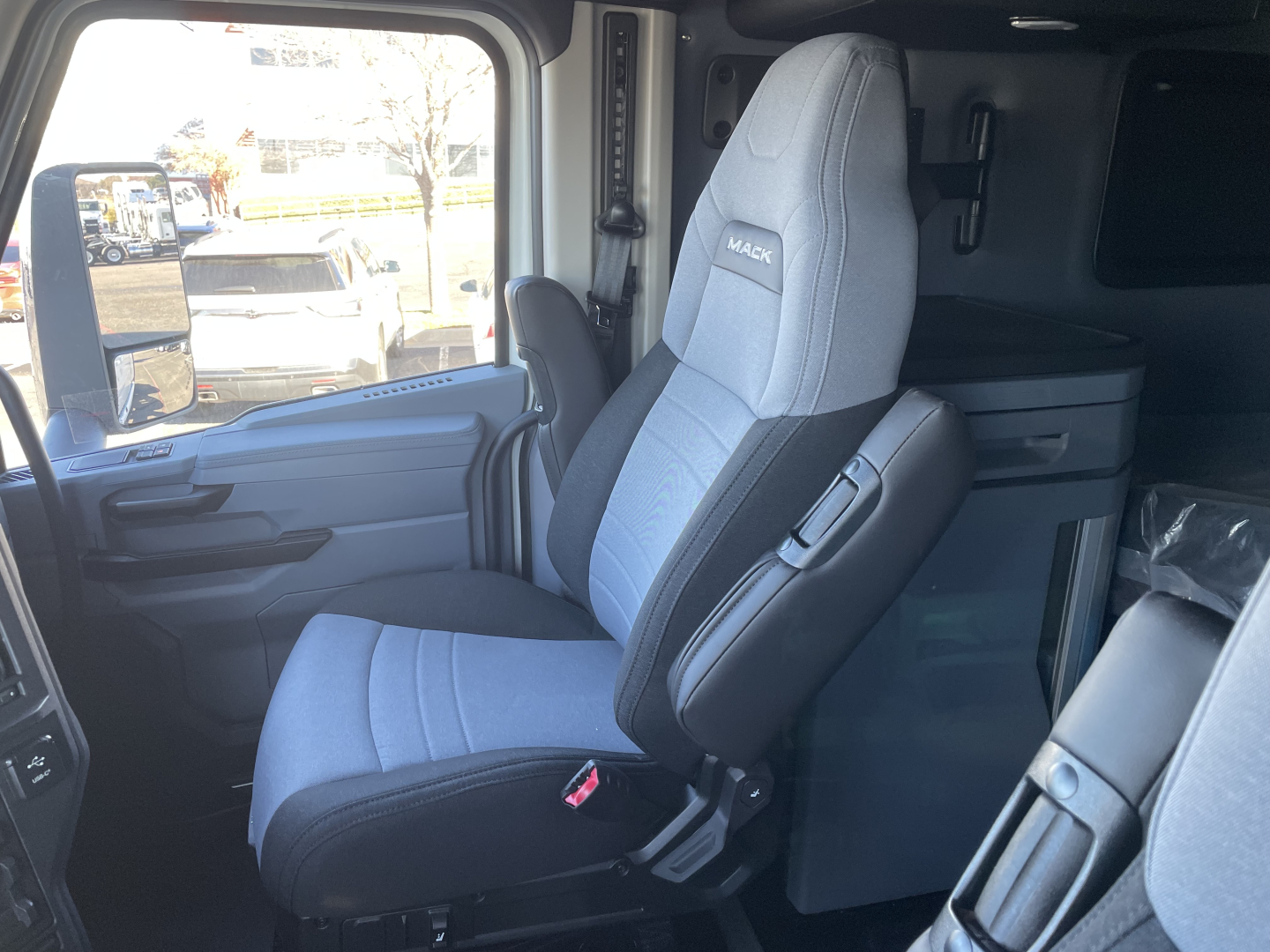 Truck cabin interior showing driver's seat with Mack branding and light gray/blue upholstery, center console, and side doorway.