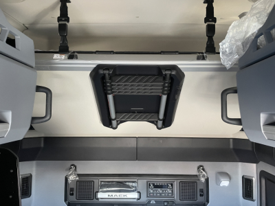 Interior view of a new Mack PR64T76H truck cab showing overhead sleeper access, dash controls, and seating mounts.