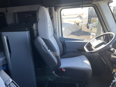 Cab interior of a Mack PR64T76H truck showing driver seat, passenger seat, steering wheel, dashboard, and bunk area in view.