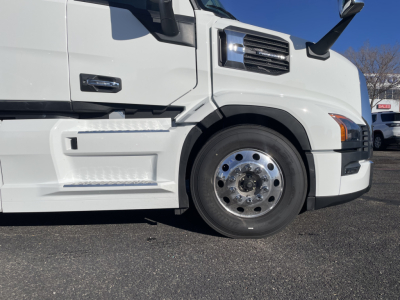 Front left side of a white Mack truck showing front wheel and cab details with PR64T76H label and chrome wheel hub.
