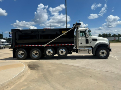 Truck side view of a new 2027 Mack GR104F dump truck showing black dump body with chrome wheels and side railing.