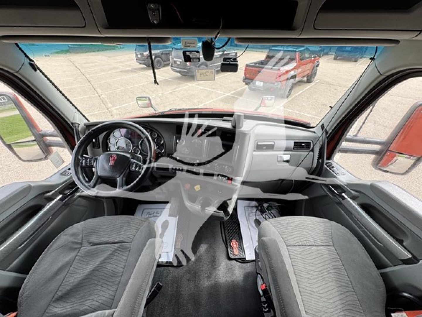 Kenworth T680 interior view of cab with steering wheel and dashboard; front windshield shows dealership lot outside.
