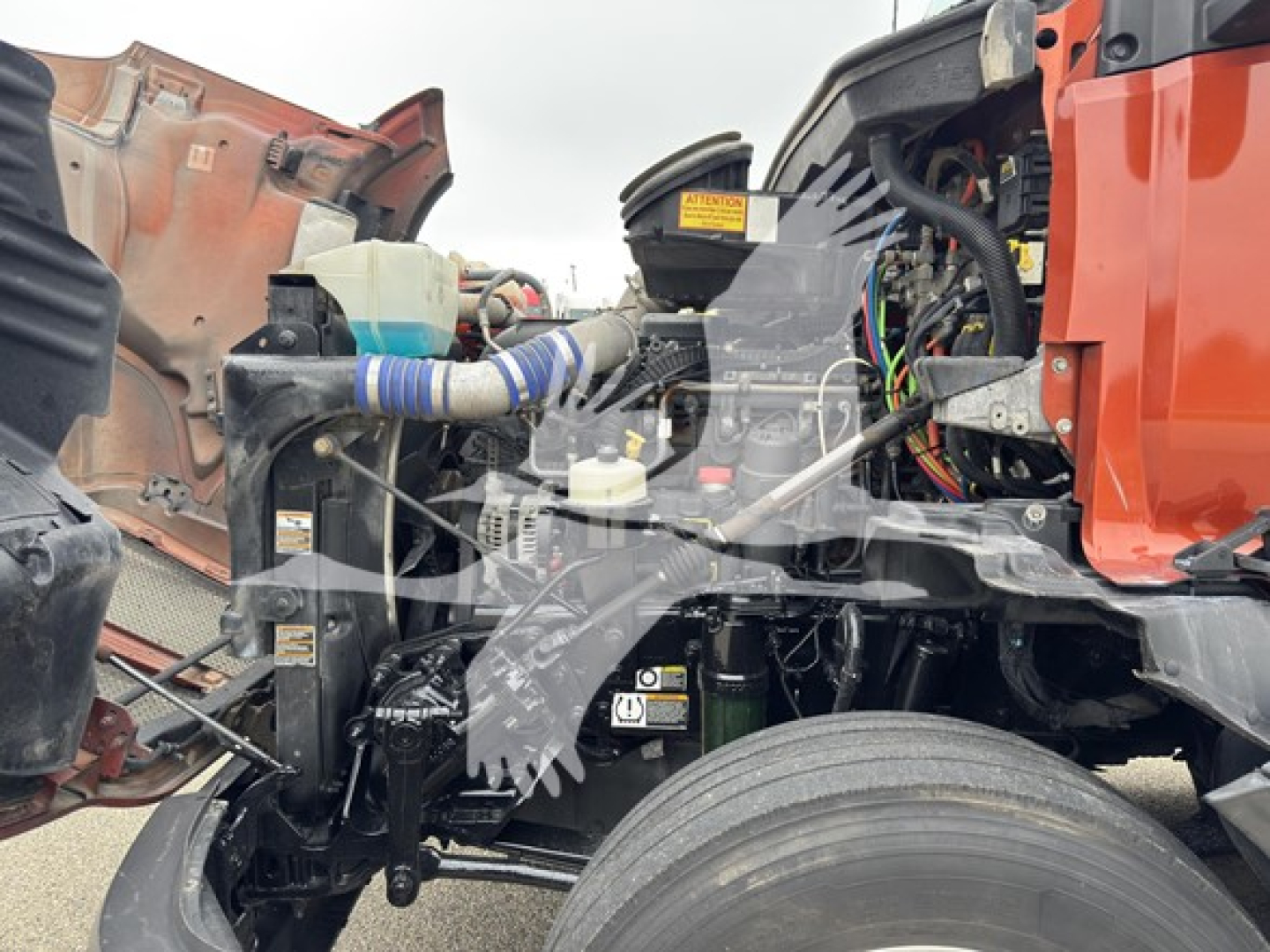 Kenworth T680 engine bay area showing coolant reservoir, hoses, wiring harness, and part of front axle assembly.