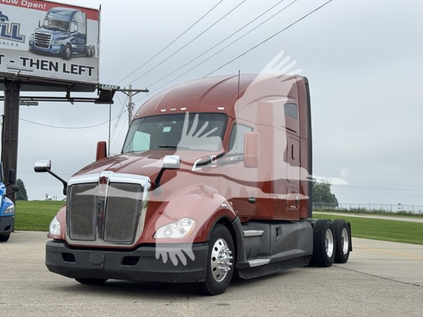 Kenworth T680 semi-truck in a yard with red cab and sleeper, dual rear axles, front grille and headlights visible.