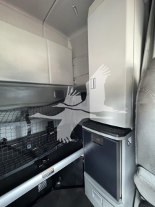 Cab interior of a 2019 Kenworth T680 sleeper truck showing storage cabinet and vertical panel in a light gray color.
