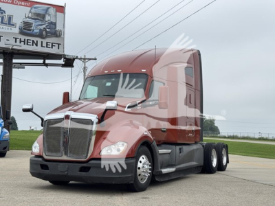 Kenworth T680 semi-truck in a yard with red cab and sleeper, dual rear axles, front grille and headlights visible.