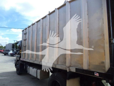 Truck cargo area showing large metal dump body with Isuzu truck chassis and side fuel tanks.