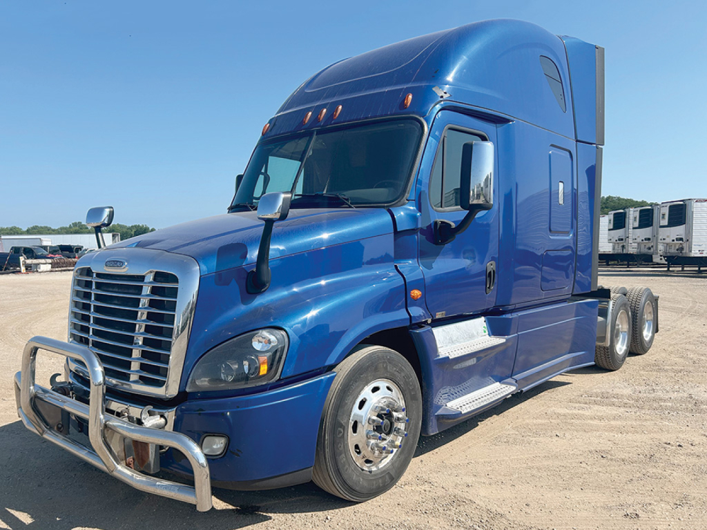 Truck cab exterior showing blue Freightliner Cascadia125 sleeper with chrome bumper and wheel guards, side step, dual rear axles, and daytime running lights.