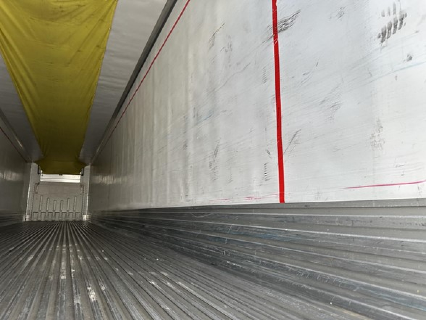 Interior of a refrigerated trailer showing ribbed metal floor and insulated walls with red stripes; yellow curtain at top.
