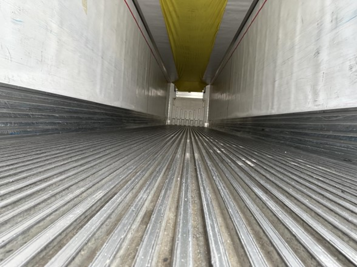 Trailer interior showing ribbed floor and walls, yellow ceiling, open end with light at far end.