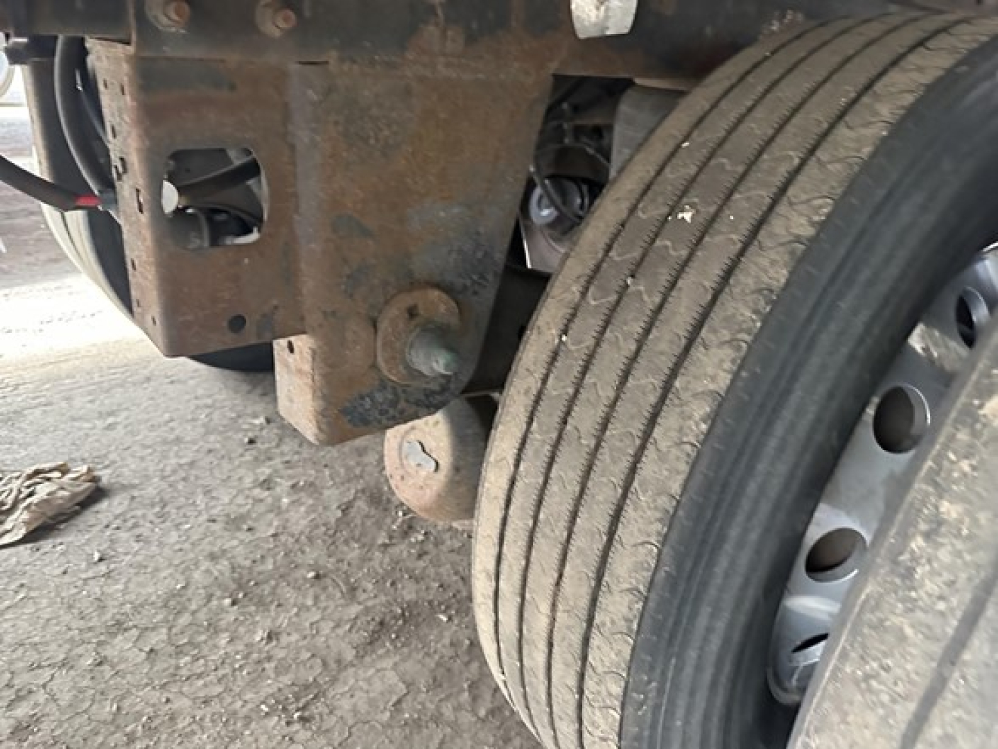 Trailer wheel and undercarriage showing suspension and twin main beam with rust and dirt.